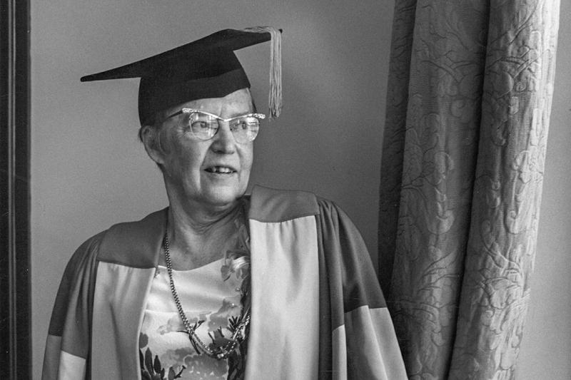 Elsie McGill smiles and looks out a window while wearing academic robes--and cat-eye glasses--in 1973.