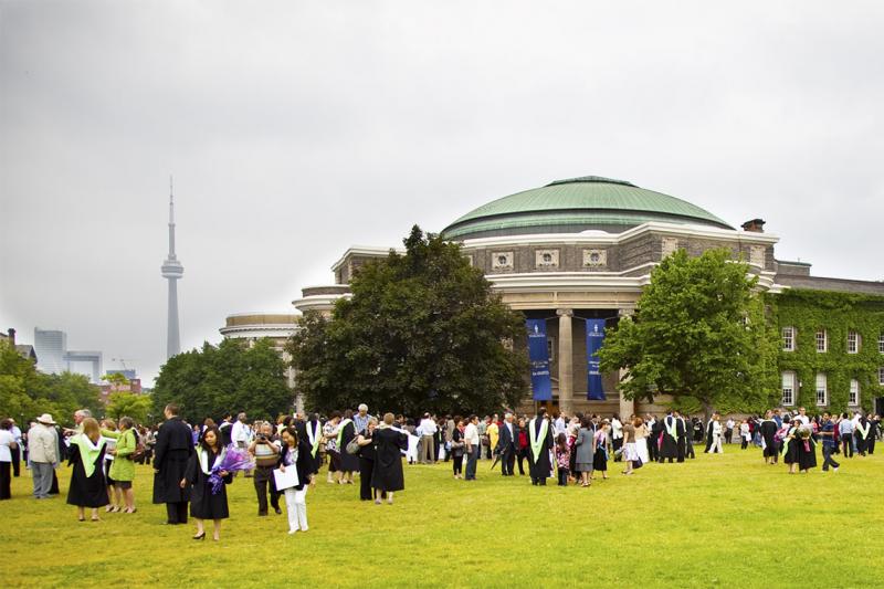 Convocation Hall in sunshine with new graduates out front on the lawn, wearing academic robes.