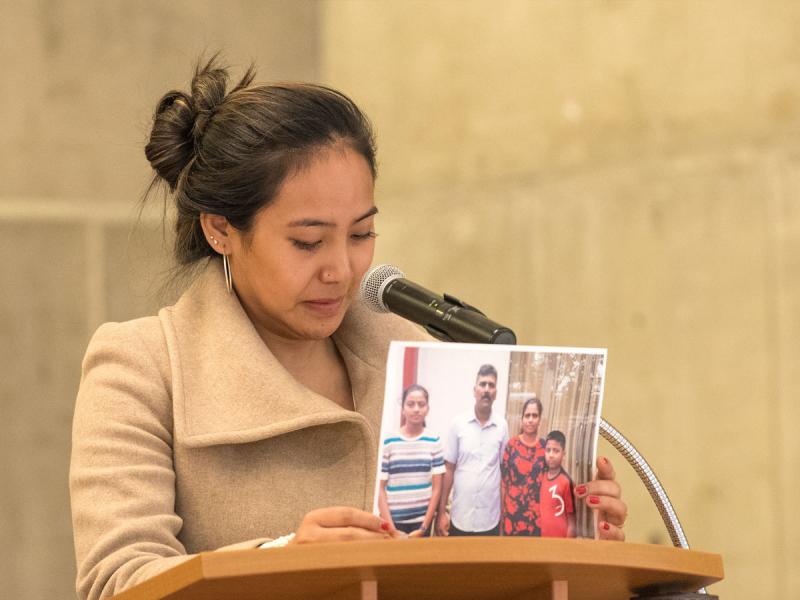 Chemi Lhamo stands at a podium, tearfully holding up a photograph of two parents with their two children. (photo by Don Campbell)