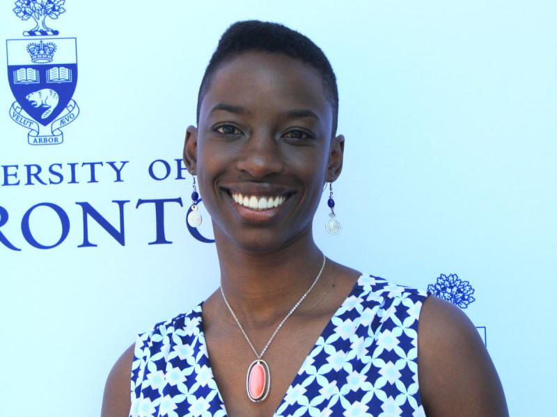Janelle Joseph smiles while standing in front of a wall with the University of Toronto logo.