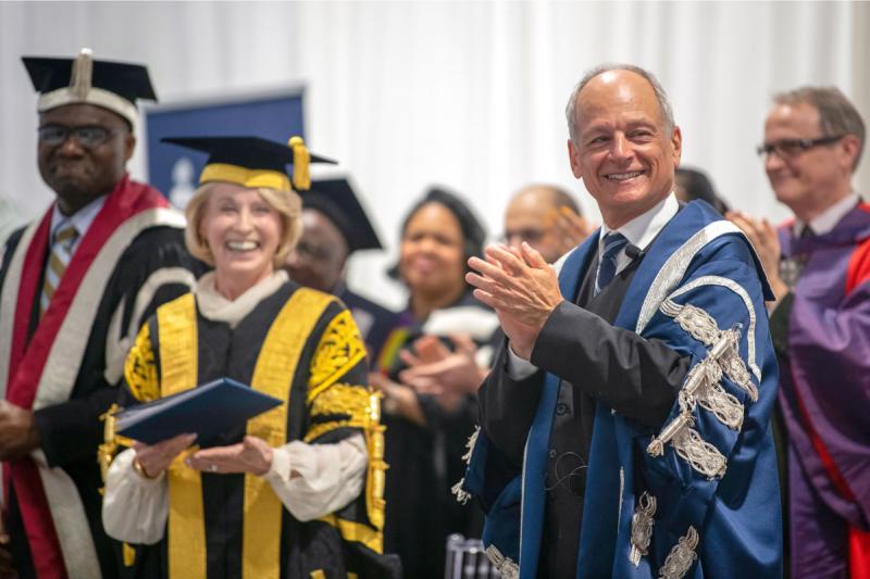 Rose Patten and Meric Gertler smile and clap, wearing academic robes.