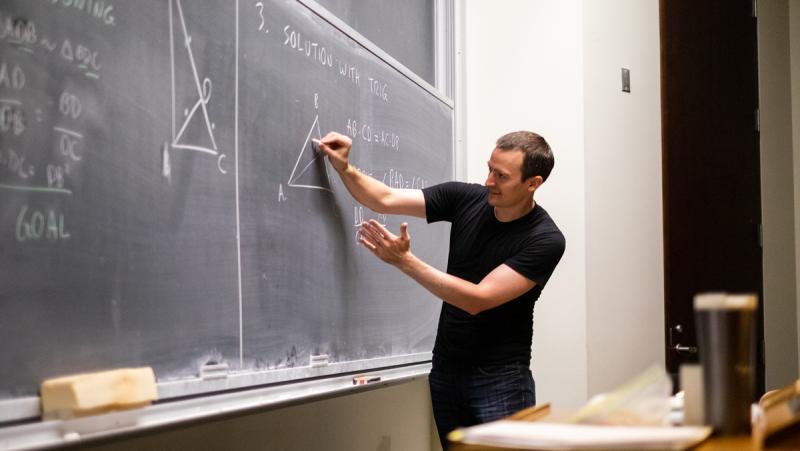 Zack Wolske gestures as he writes a geometry problem on a chalkboard.