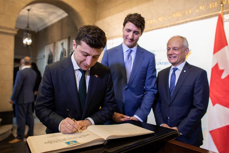Volodymyr Zelenskyy signs U of T's guest book Prime Justin Trudeau and  Meric Gertler look on.