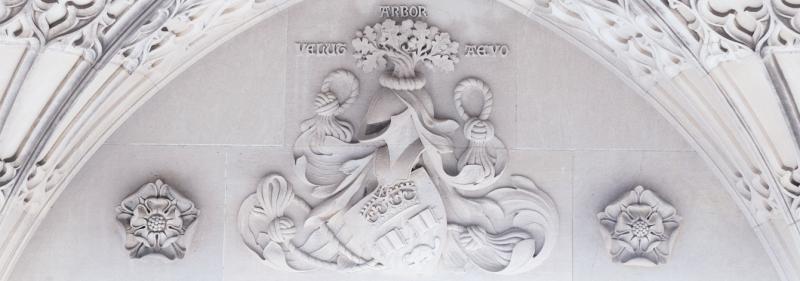 A close-up of the carved stone on the Soldiers' Tower memorial wall shows the U of T crest with tree, helmet, shield and knotted rope.