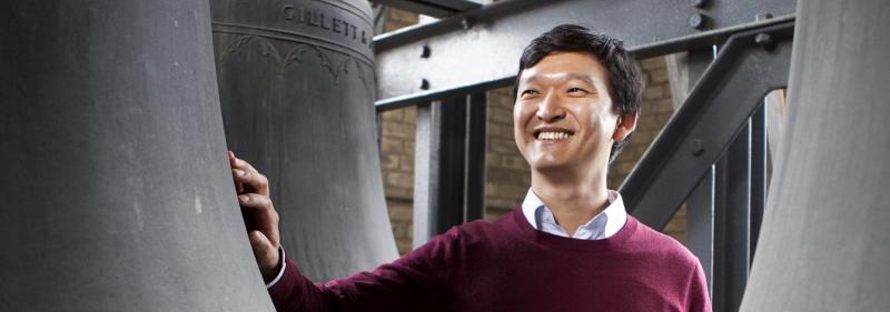 Carillonneur Roy Lee stands between giant bronze bells, smiling. (Image by Michelle Yee Photography.)