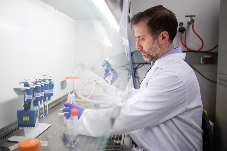 Robert Kozak, wearing gloves, transfers a liquid through a tube into a beaker.