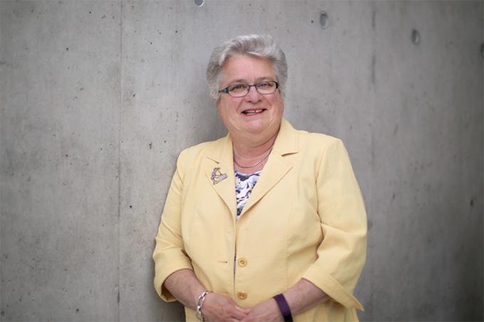 Andrea Sass-Kortsak smiling while standing by a wall, indoors. (photo by Nick Iwanyshyn)