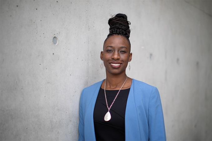 Janelle Joseph smiling while standing next to a wall, indoors. (photo by Nick Iwanyshyn)