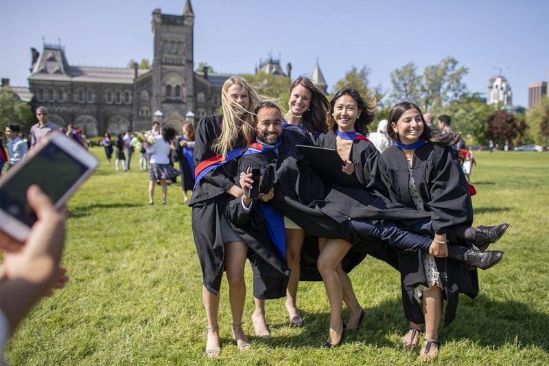 Four laughing women graduates hoist up a male graduate on Front Campus.