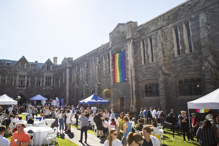 The courtyard at Hart House is packed with tents, tables and people socializing under the multicoloured Pride flag.