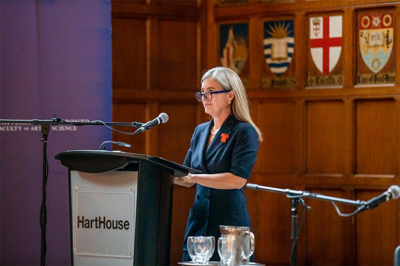 Melanie Woodin speaking at a podium and wearing an Orange Shirt Day brooch.