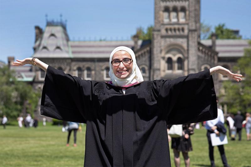 Noura Al-Jizawi, in academic robes, stretches out her arms and smiles, in front of University College.