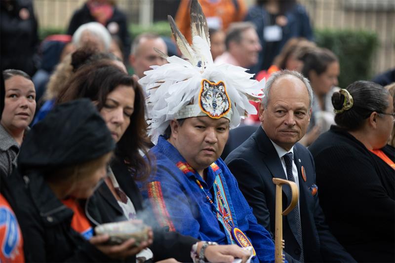 Skahendowaneh Swamp, wearing a traditional Indigenous feathered headdress, sits in the front row at the ceremony next to President Gertler.