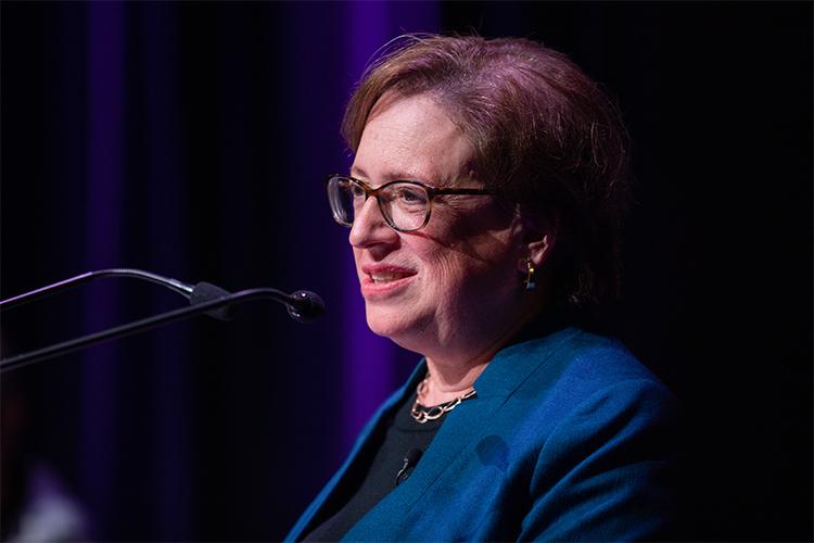 Elena Kagan smiles and speaks at a podium.