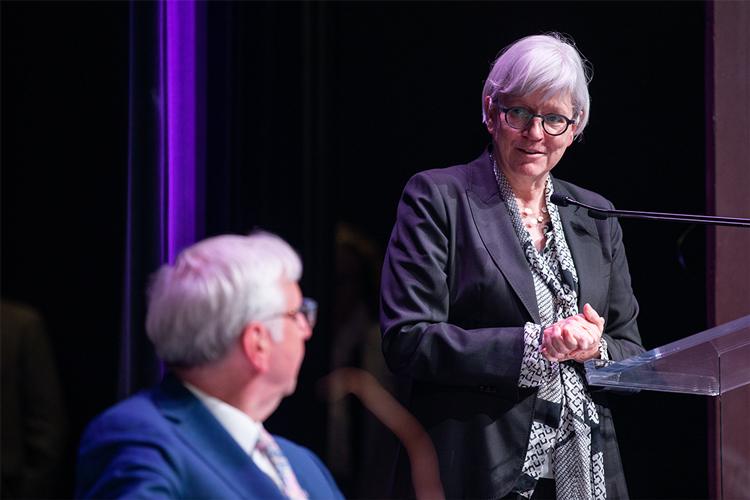 Jutta Brunnée turns from a podium to smile at distinguished guests.