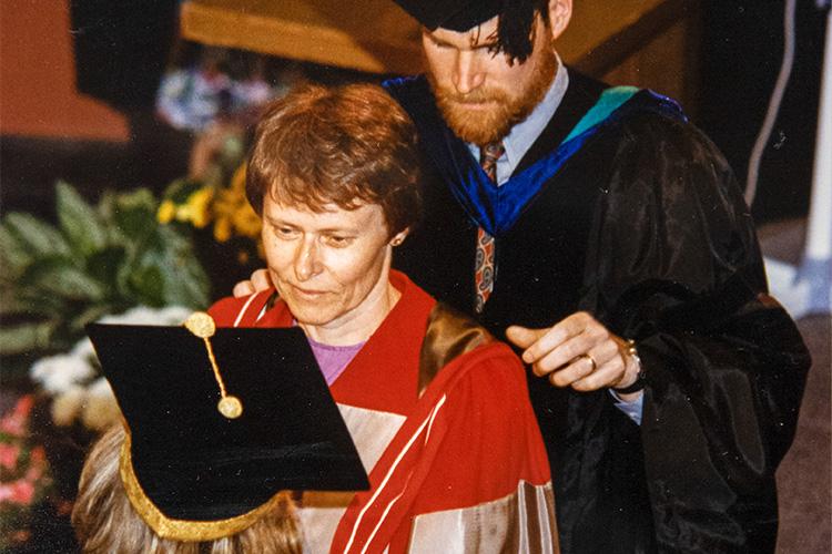 Roberta Bondar is seen from above on stage at Convocation Hall as a man settles her academic hood on her shoulders.