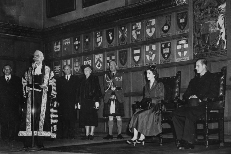 In a photo from 1951, a young Princess Elizabeth and Prince Philip sit in carved chairs in Hart House, listening to a speech.