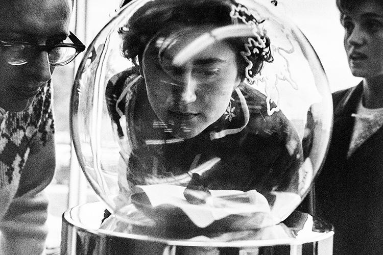 A woman peers into a glass bubble that encases a small rock and a tiny vial.