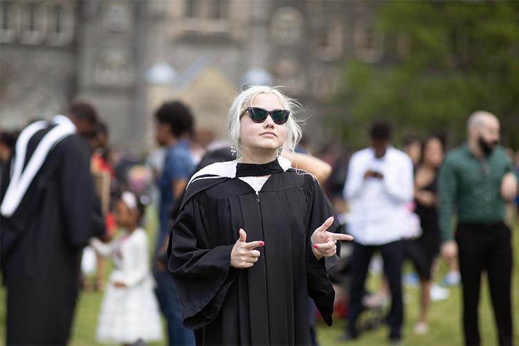 Elspeth Arbow, wearing gown, hood and sunglasses, makes finger guns on Front Campus.