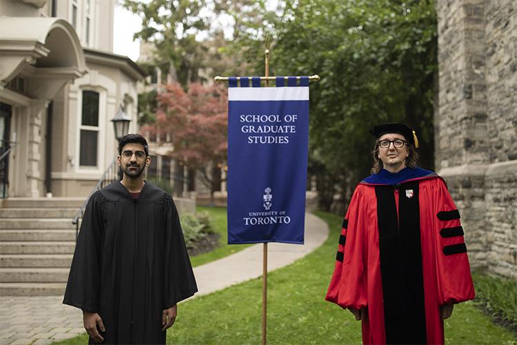Faraz Alidina and Joshua Barker, both wearing robes, stand beside a banner that reads: School of Graduate Studies.