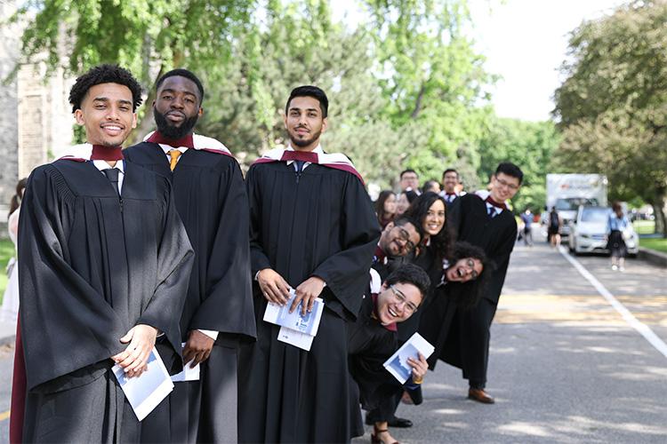 Gowned students in a line lean sideways and make happy faces.