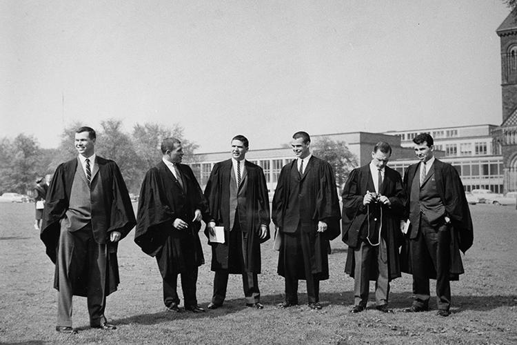 Six young men in academic robes, all looking in different directions, stand on Front Campus.