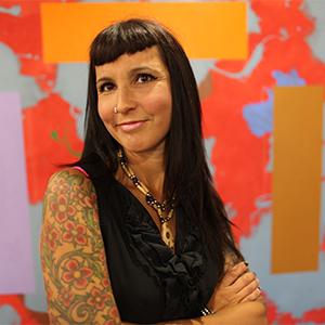 Suzanne Stewart smiles as she stands in front of an abstract mural.