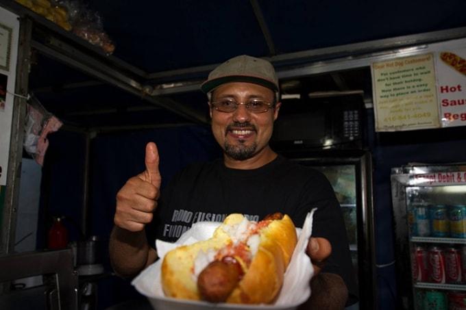 Nasir holds up a hot dog at his stand. (photo by U of T Drizzy) 