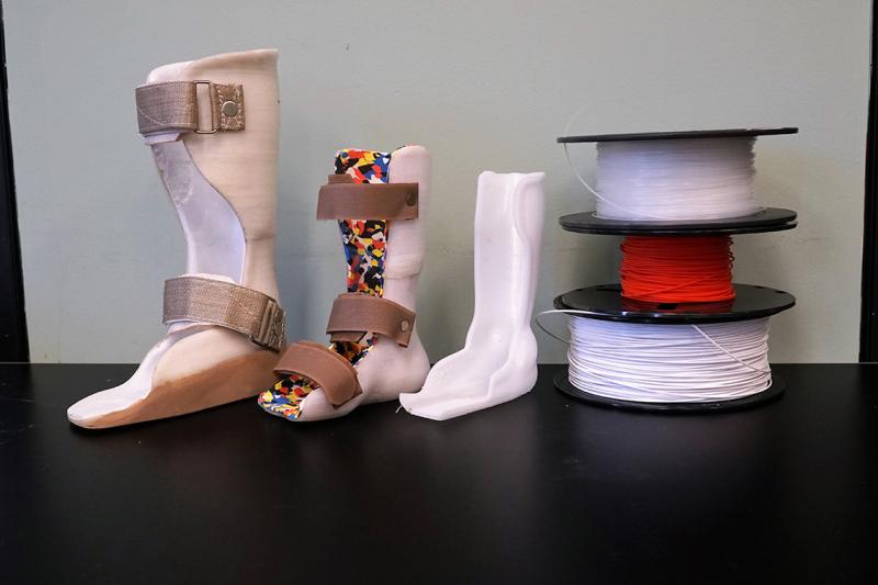 Three differently sized walking boots stand next to a stack of reels of 3D printing filament.