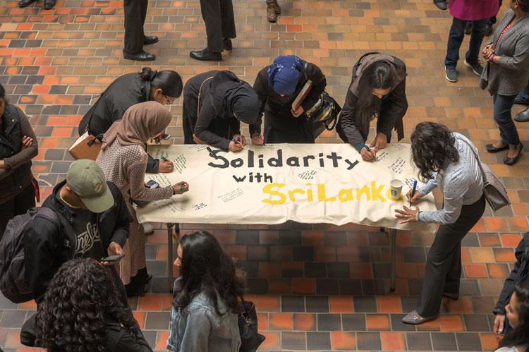Looking from above, we see people gathered round a large table signing a banner that reads "Solidarity with Sri Lanka"
