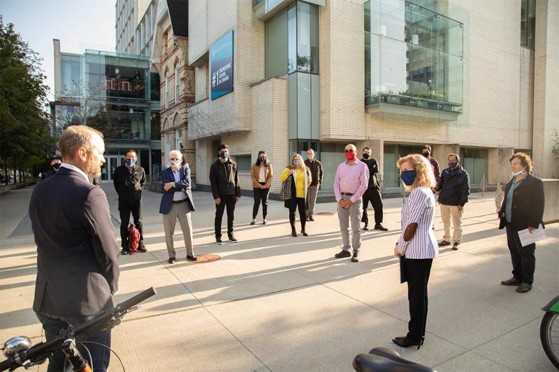 Mike Layton speaks to a group of people wearing masks and scattered over a small plaza.