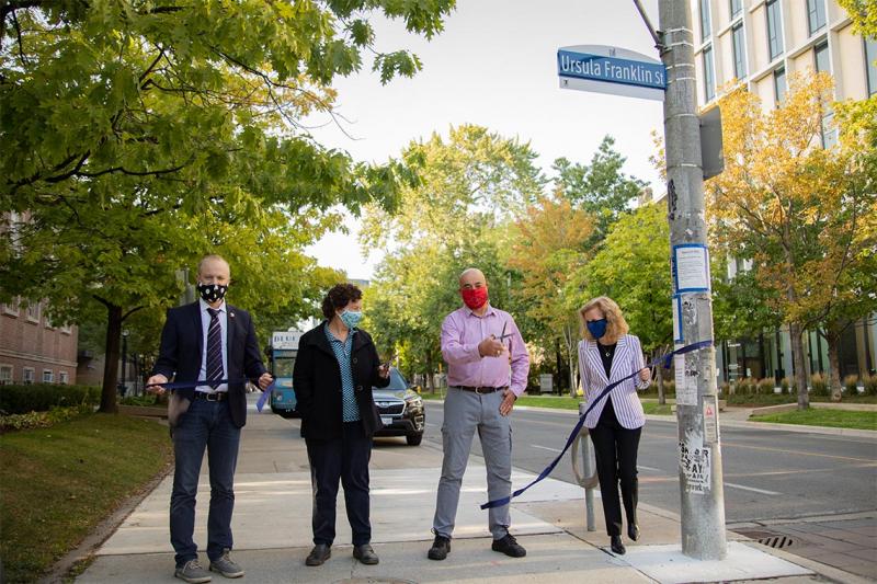 Son Martin Franklin, wearing a mask, cuts a blue ribbon tied to a street sign.