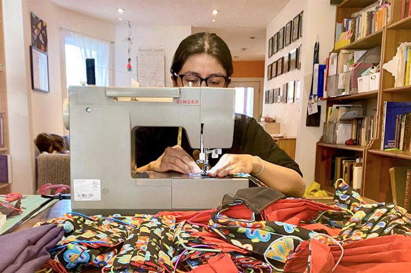 Fernanda Yanchpaxi works on her sewing machine, surrounded by piles of fabric masks.