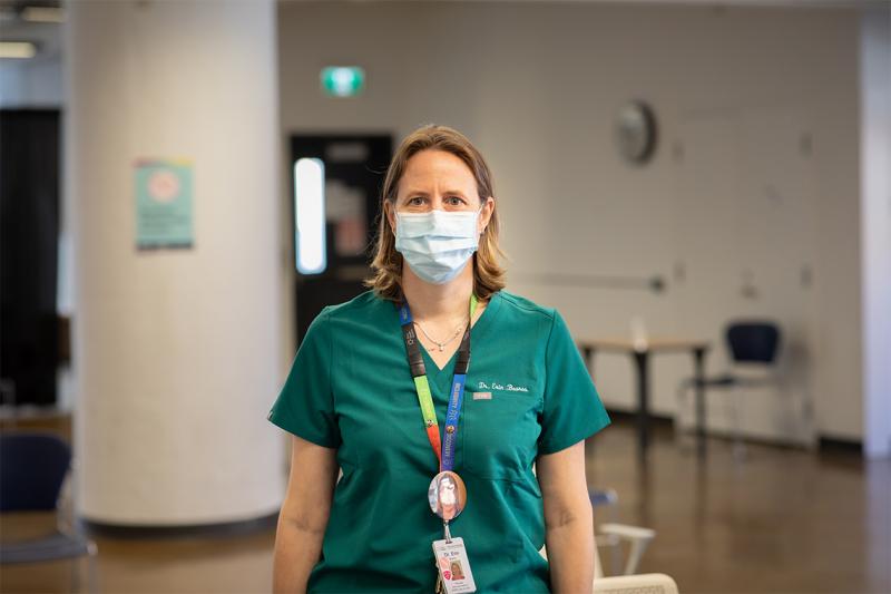 Erin Bearss, wearing a mask and scrubs, stands in a hall.