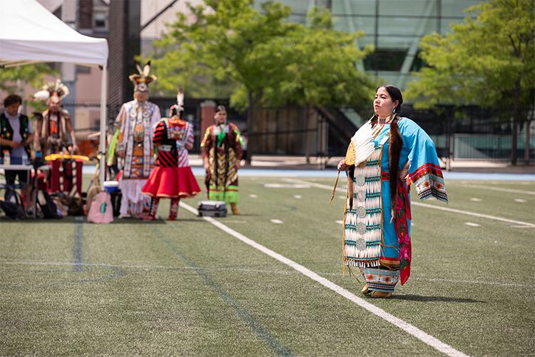 Marionne Rutledge on the turf at Varsity Stadium, wearing regalia and holding a feather fan.