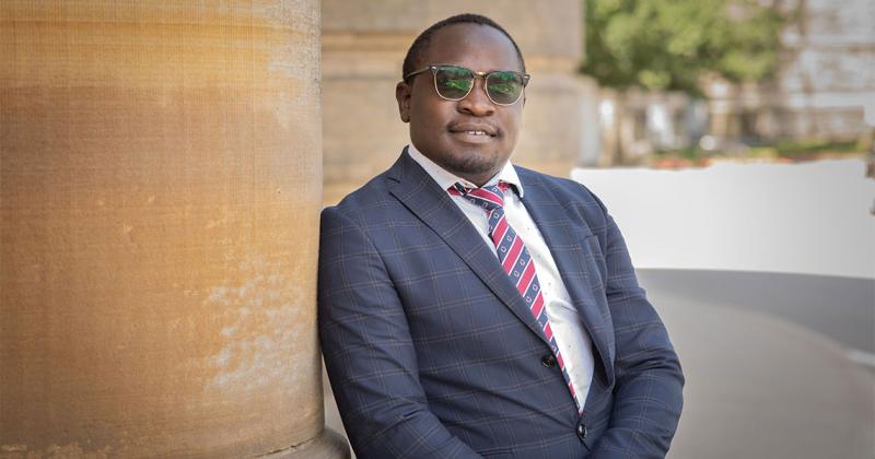 Michael Samakayi  smiles as he leans on a pillar outside Convocation Hall.