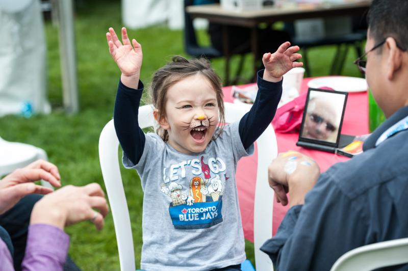 Small child with face paint to look like a lion, growling ferociously with arms in the air