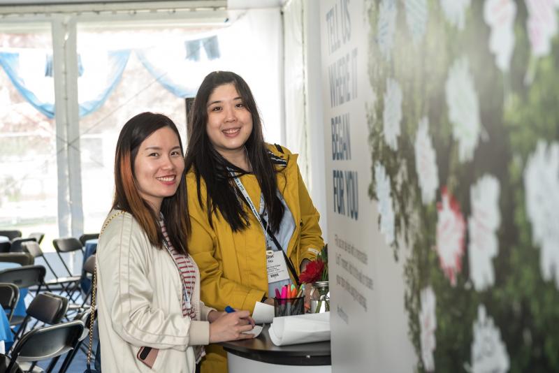 Two smiling alum getting ready to fill out their experiences for the Alumni Reunion experiential wall using paper and markers