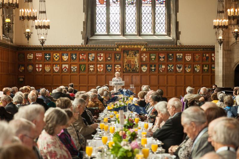 Chancellor Rose Patten stands at lectern in front of crowd of alumni seated at long tables