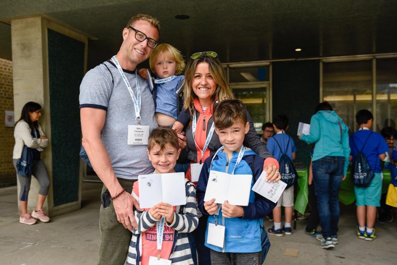 Two parents and three young children with their arms around each other. The children are proudly holding open their Alumni Reunion passports