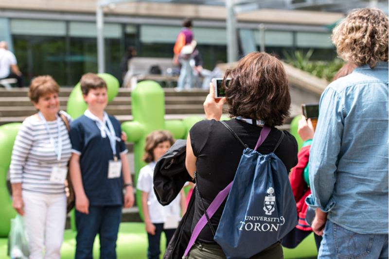 People take pictures as others pose in front of a large sign that says U of T Reunion.