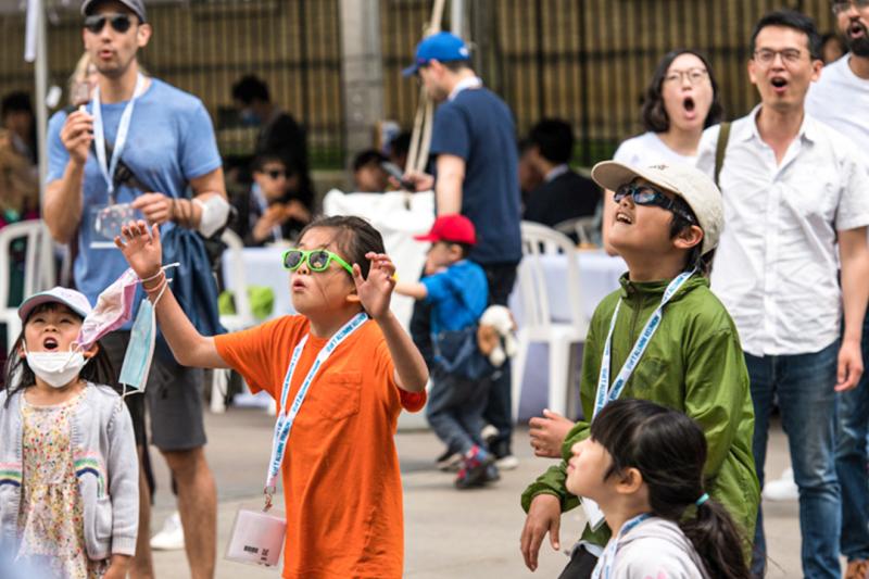 Kids and adults look upwards as their mouths drop open in surprise.