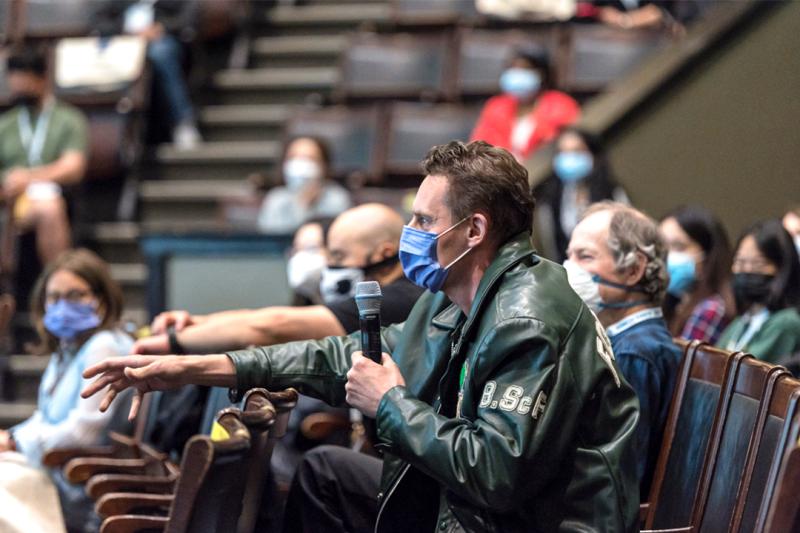 An audience member in a lecture theatre takes a microphone to ask a question.