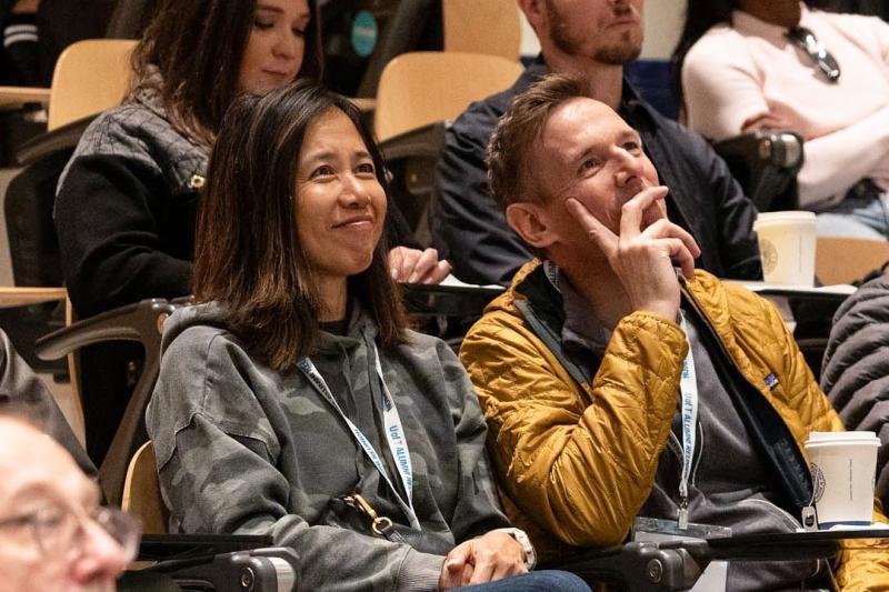 Two alumni listening attentive to the lecture while smiling.