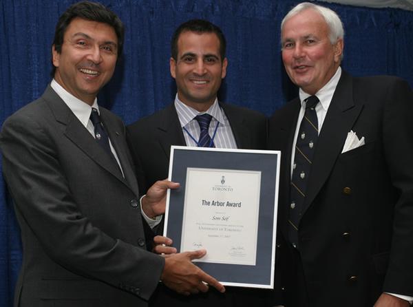 Som Seif smiles as he holds a framed award and poses with U of T president David Naylor.
