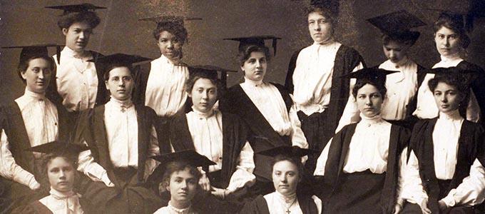 Myrtle Burgess stands in the back row of a group of women, all wearing mortarboards and Edwardian dresses.