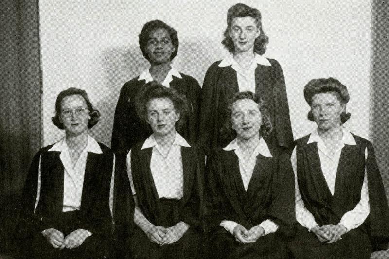 Gloria Carpenter smiles as she poses with five other women. All wear 1940s hairdos and academic gowns.