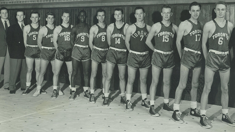 A row of young men wearing old-fashioned basketball shorts and singlets.