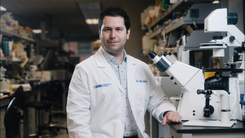 Brian Ballios sits in a lab coat, in front of a microscope
