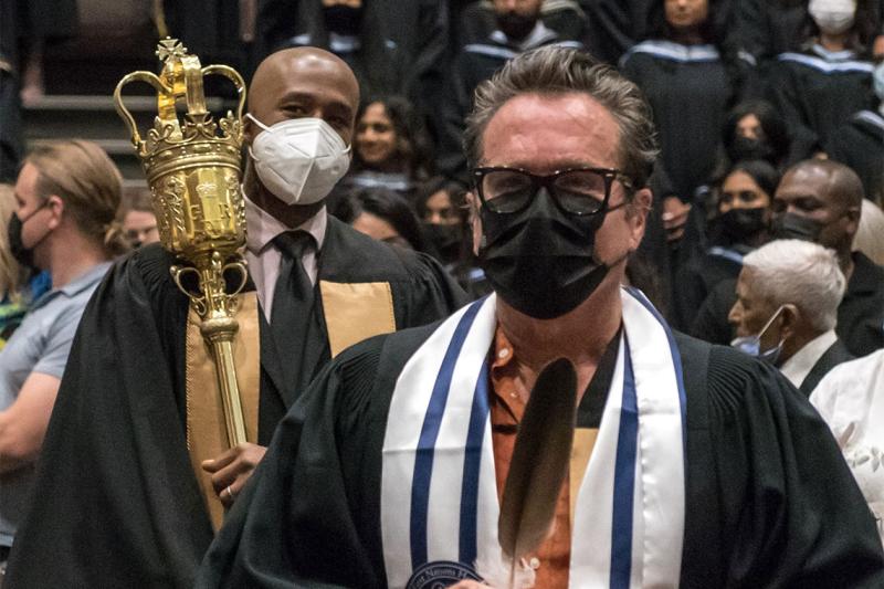 John Croutch, wearing a two-row wampum belt scarf, carries an eagle feather in a convocation procession.